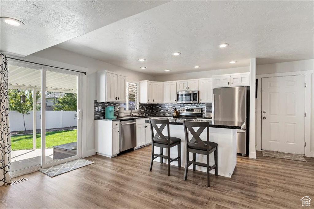 Kitchen with stainless steel appliances, white cabinetry, wood-type flooring, and a kitchen bar