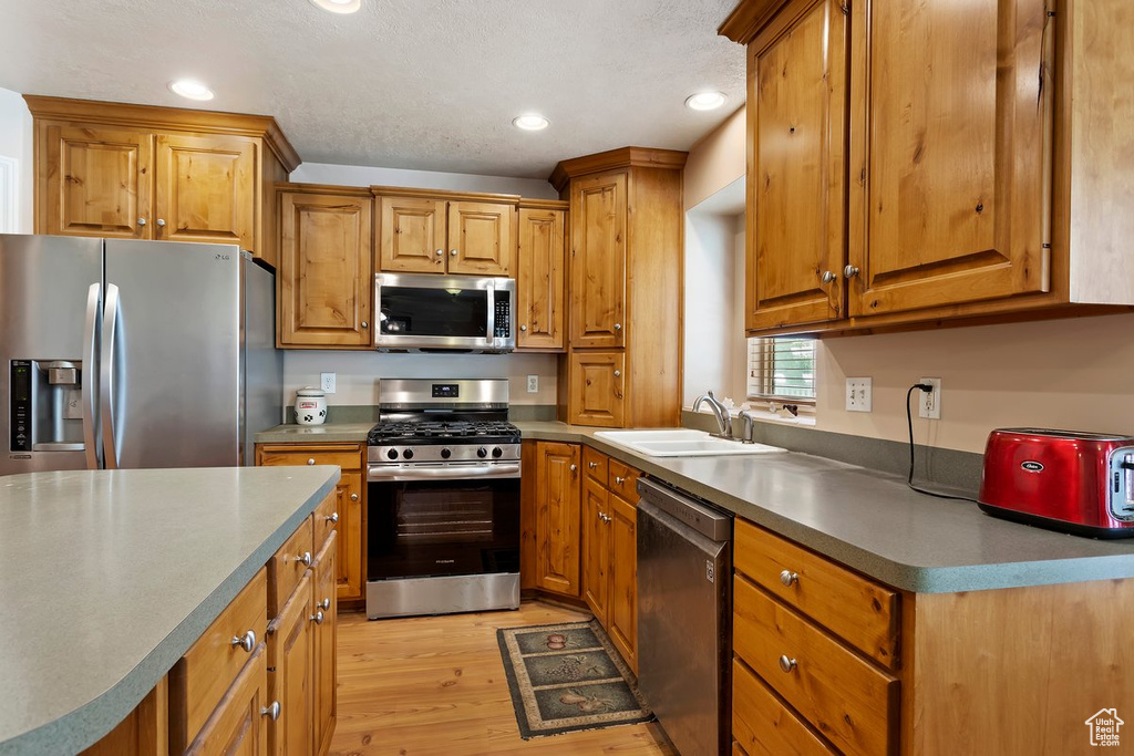 Kitchen featuring stainless steel appliances, a textured ceiling, light wood-type flooring, and sink