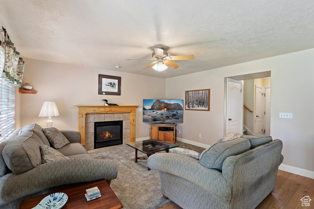 Living room with ceiling fan, a textured ceiling, a fireplace, and wood-type flooring