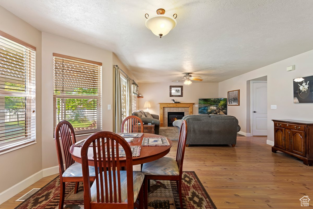 Dining area with ceiling fan, a tile fireplace, hardwood / wood-style flooring, and a textured ceiling