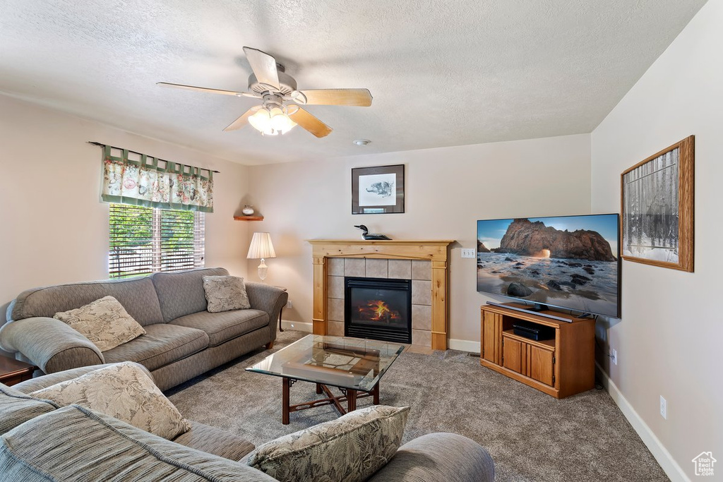 Carpeted living room with a textured ceiling, a tile fireplace, and ceiling fan