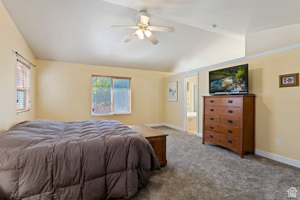 Carpeted bedroom featuring connected bathroom, vaulted ceiling, ceiling fan, and multiple windows