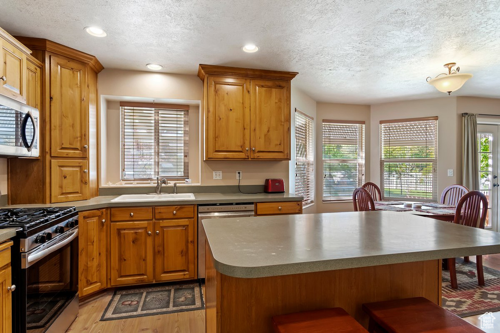 Kitchen with sink, a kitchen island, a textured ceiling, stainless steel appliances, and light wood-type flooring