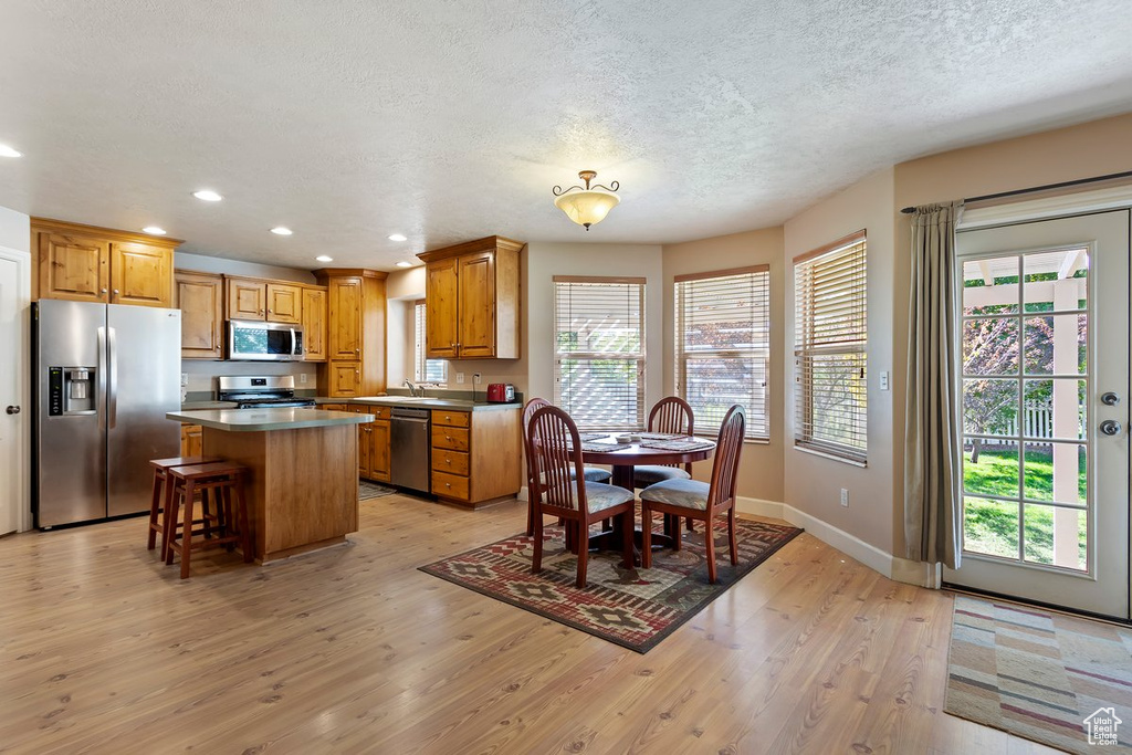 Kitchen featuring a wealth of natural light, light wood-type flooring, a kitchen island, a kitchen breakfast bar, and stainless steel appliances