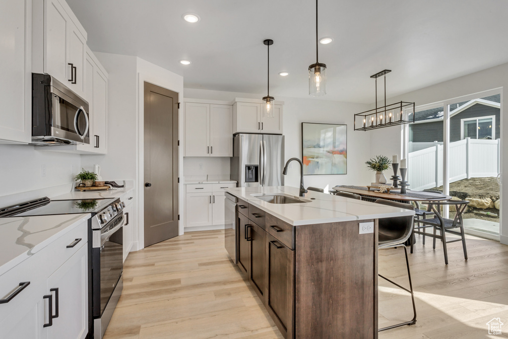 Kitchen featuring an island with sink, white cabinets, stainless steel appliances, light wood-type flooring, and sink