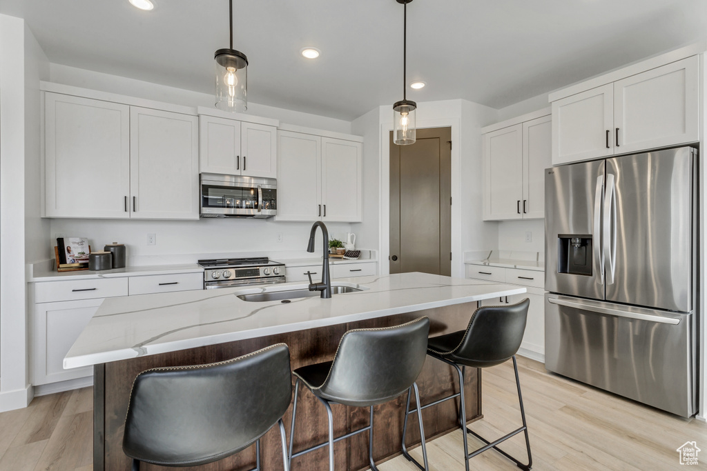 Kitchen with appliances with stainless steel finishes, an island with sink, light stone counters, light wood-type flooring, and sink