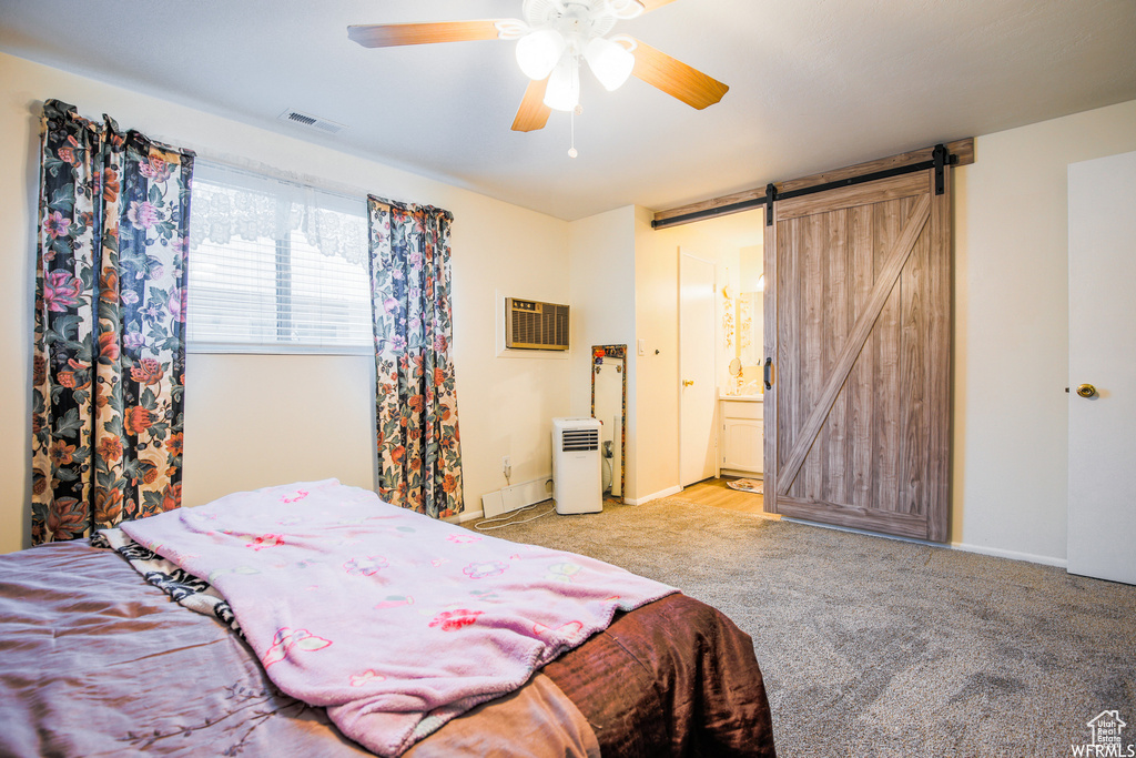 Carpeted bedroom with an AC wall unit, connected bathroom, ceiling fan, and a barn door