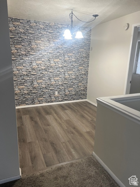 Spare room with a textured ceiling, a chandelier, and dark wood-type flooring