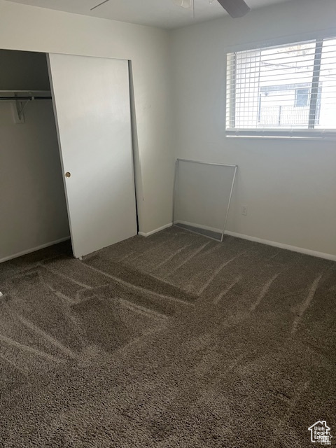 Unfurnished bedroom featuring ceiling fan, a closet, and dark carpet