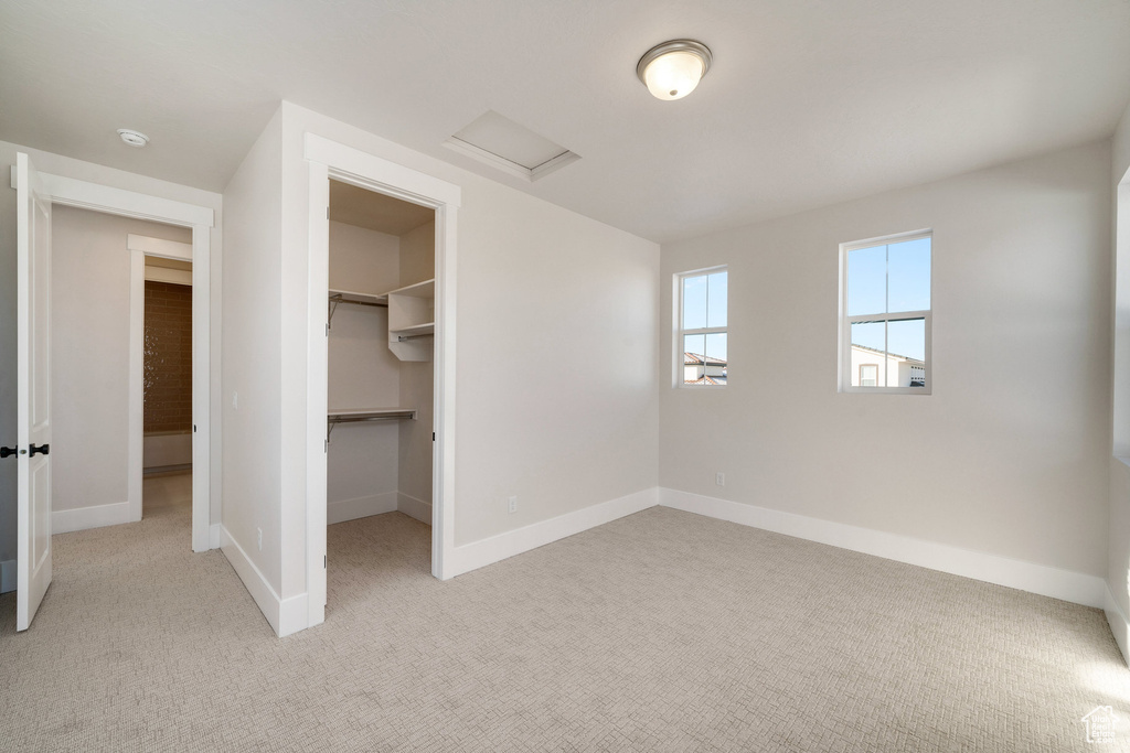 Unfurnished bedroom with a spacious closet, light colored carpet, and a closet