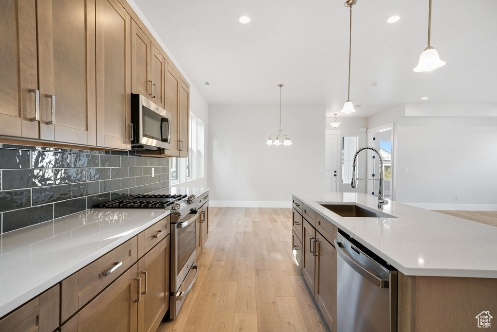 Kitchen featuring light hardwood / wood-style floors, a large island, stainless steel appliances, decorative light fixtures, and sink