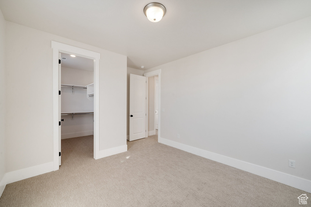 Unfurnished bedroom featuring a spacious closet, a closet, and light carpet