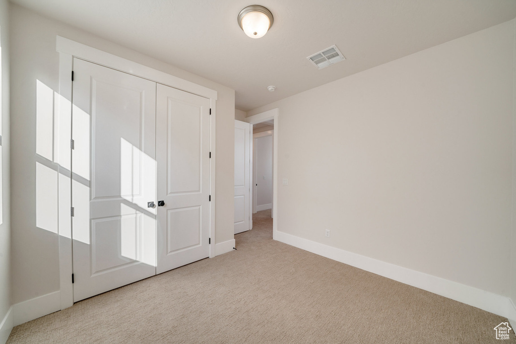 Unfurnished bedroom featuring light carpet and a closet