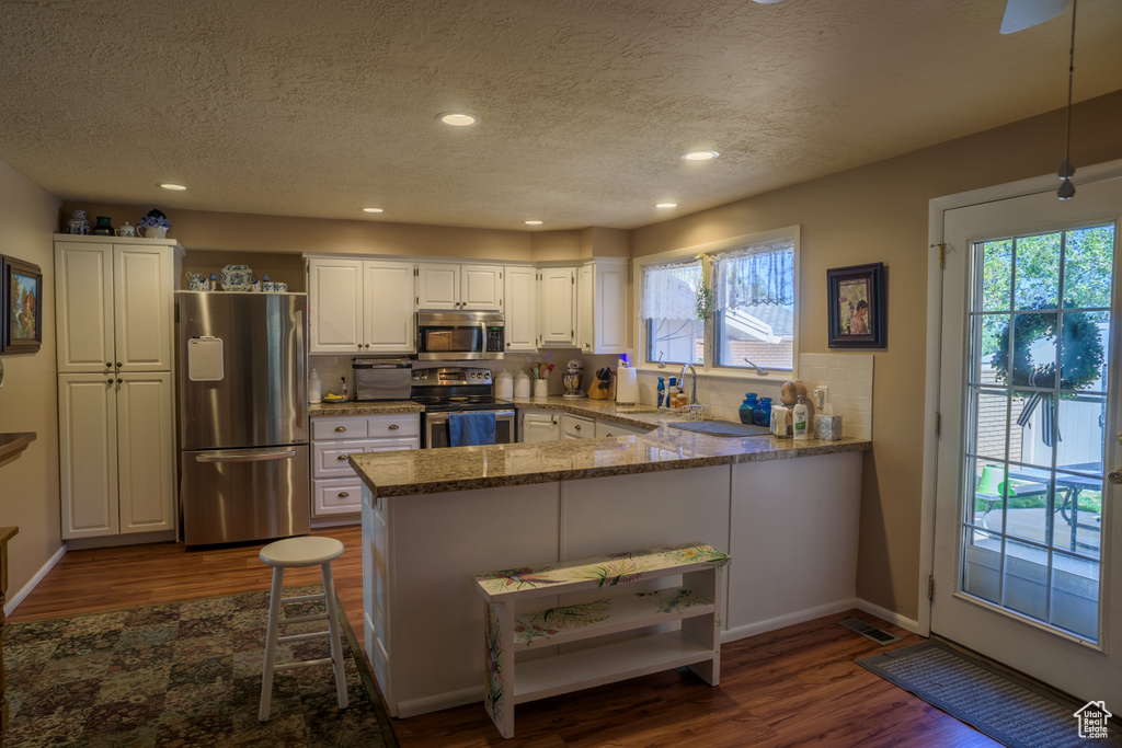 Kitchen with stainless steel appliances, white cabinetry, kitchen peninsula, and dark wood-type flooring