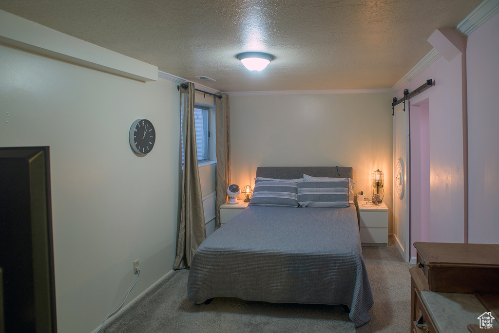 Bedroom with a barn door, crown molding, a textured ceiling, and light carpet