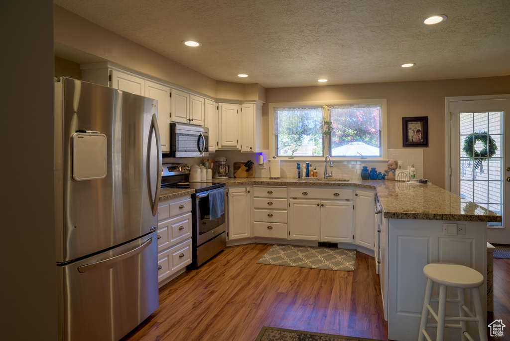 Kitchen featuring wood-type flooring, white cabinets, appliances with stainless steel finishes, and kitchen peninsula