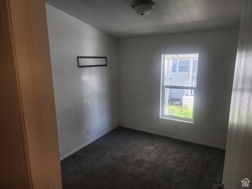 Empty room with dark colored carpet, healthy amount of natural light, and baseboards