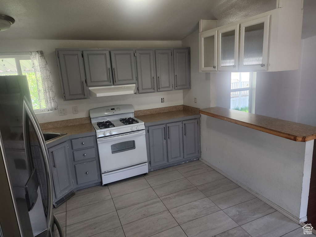 Kitchen with white range with gas cooktop, gray cabinetry, stainless steel refrigerator with ice dispenser, and under cabinet range hood
