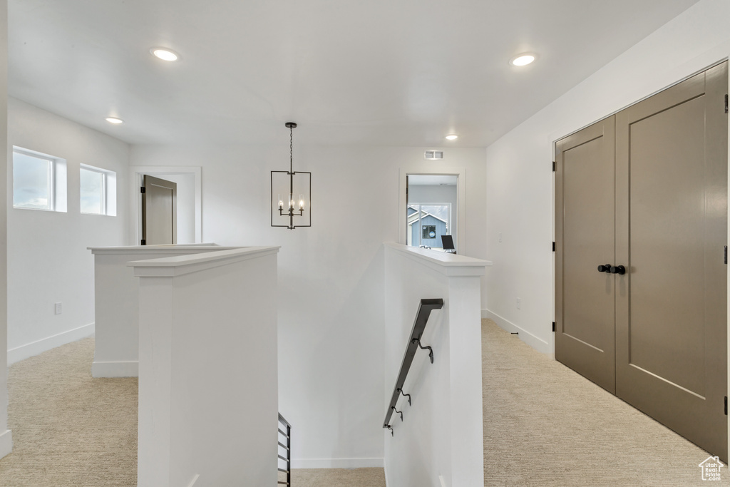 Corridor with light carpet and a notable chandelier