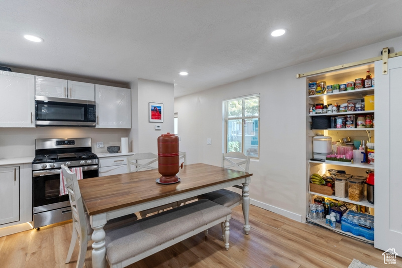 Kitchen with appliances with stainless steel finishes, a barn door, light hardwood / wood-style floors, and white cabinets