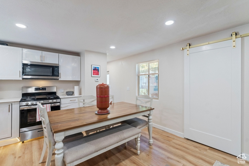 Kitchen featuring appliances with stainless steel finishes, a barn door, light wood-type flooring, and white cabinets