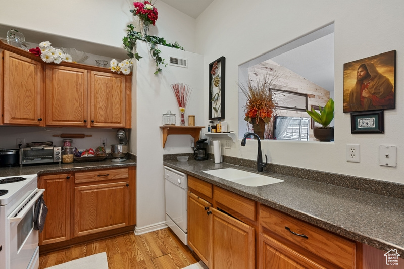 Kitchen featuring lofted ceiling, sink, white appliances, dark stone countertops, and light hardwood / wood-style floors