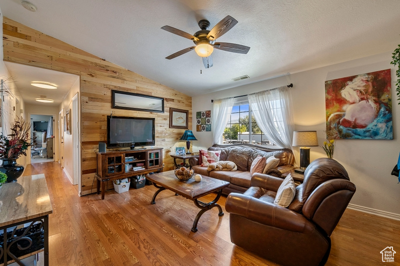 Living room with a textured ceiling, hardwood / wood-style flooring, vaulted ceiling, wooden walls, and ceiling fan