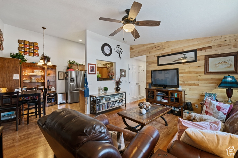 Living room featuring light wood-type flooring, wooden walls, ceiling fan, and high vaulted ceiling