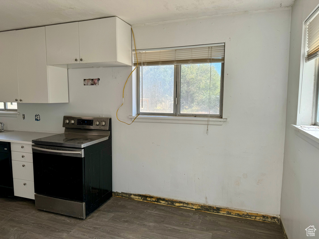 Kitchen with stainless steel electric stove, dark hardwood / wood-style floors, and white cabinets