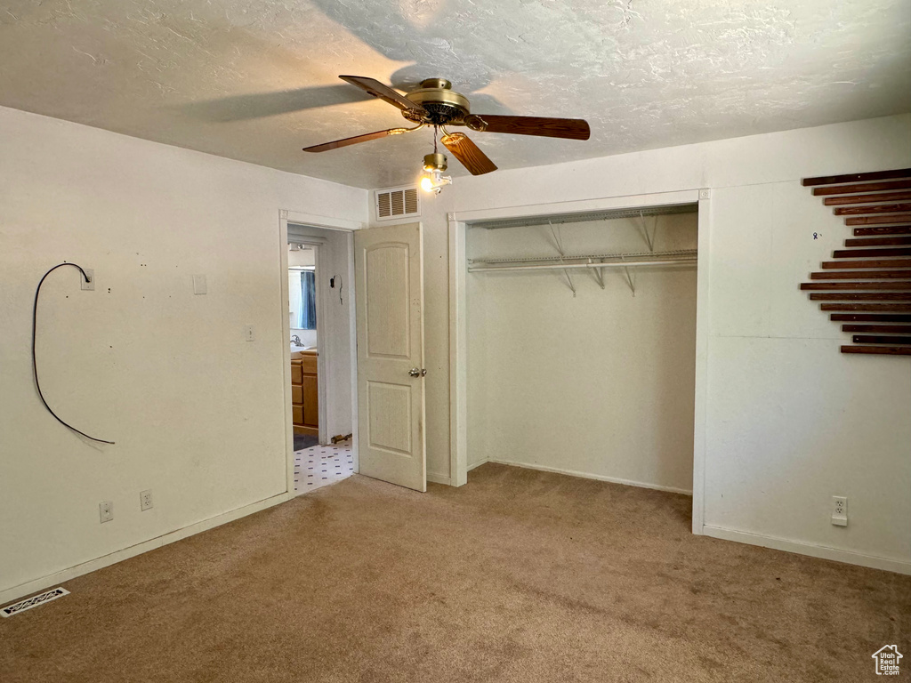 Unfurnished bedroom featuring a closet, light colored carpet, ceiling fan, and a textured ceiling