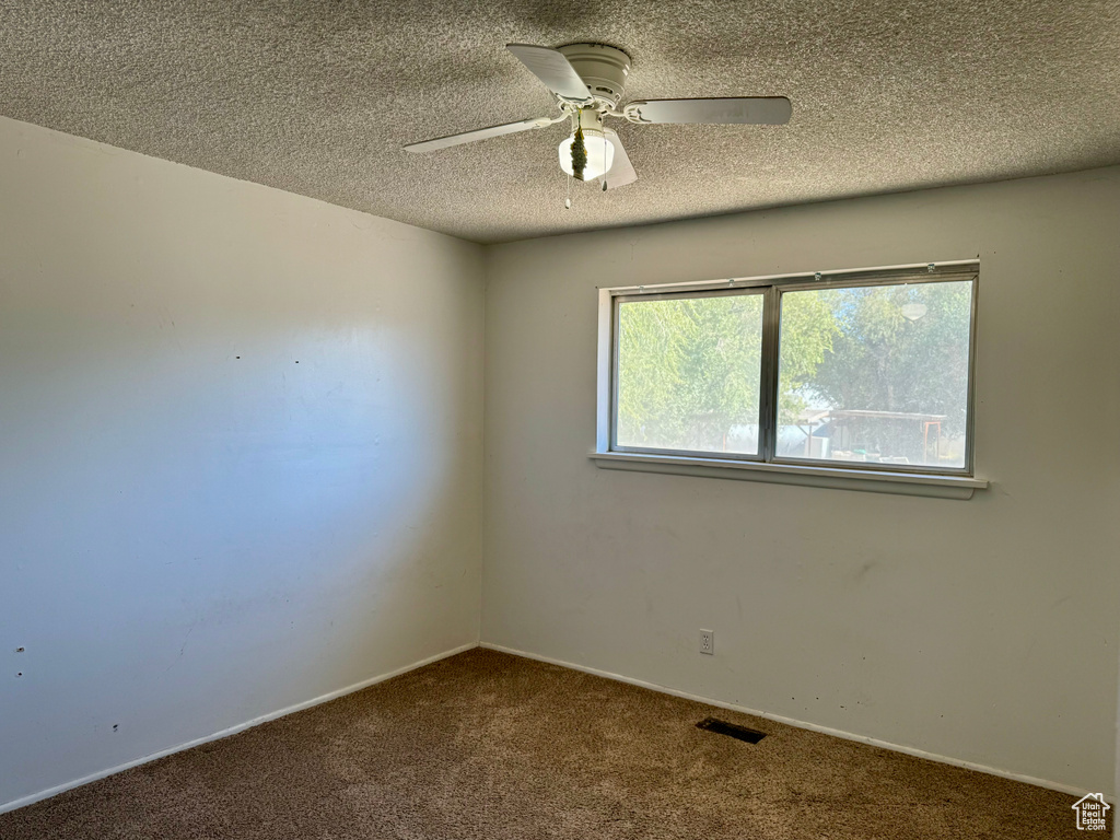 Carpeted empty room featuring ceiling fan and a textured ceiling