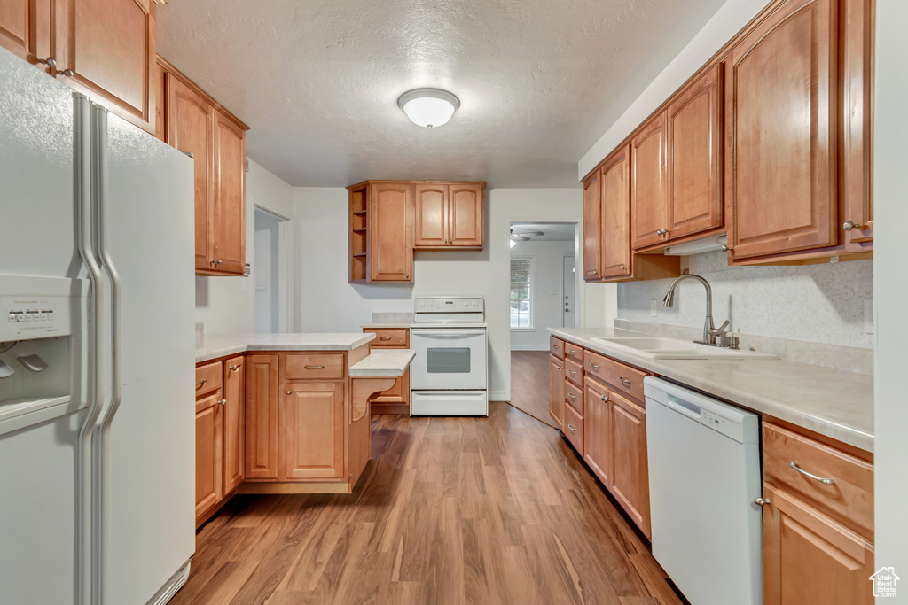 Kitchen featuring a textured ceiling, white appliances, hardwood / wood-style floors, and sink