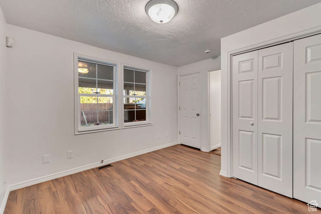 Unfurnished bedroom with a closet, hardwood / wood-style flooring, and a textured ceiling