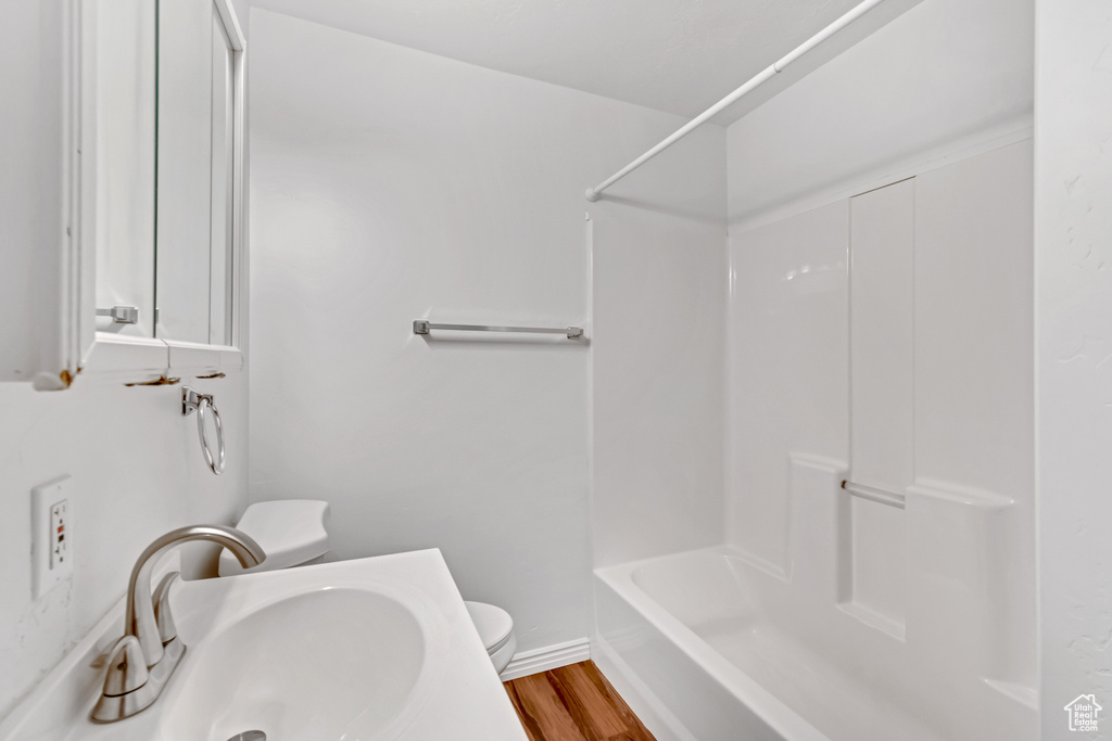 Full bathroom featuring wood-type flooring, shower / washtub combination, sink, and toilet