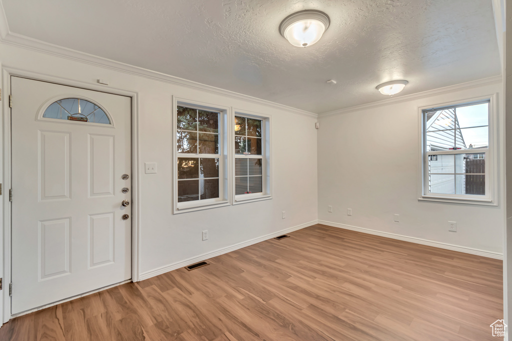 Foyer entrance featuring ornamental molding, a textured ceiling, and light hardwood / wood-style floors