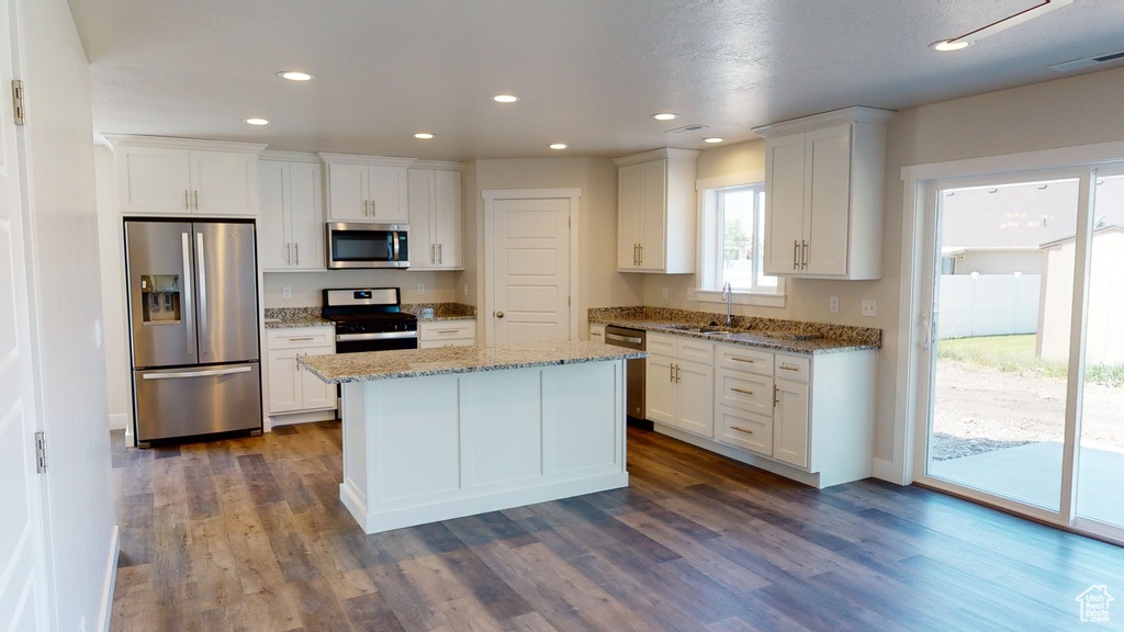 Kitchen featuring light stone countertops, white cabinets, appliances with stainless steel finishes, and dark wood-type flooring