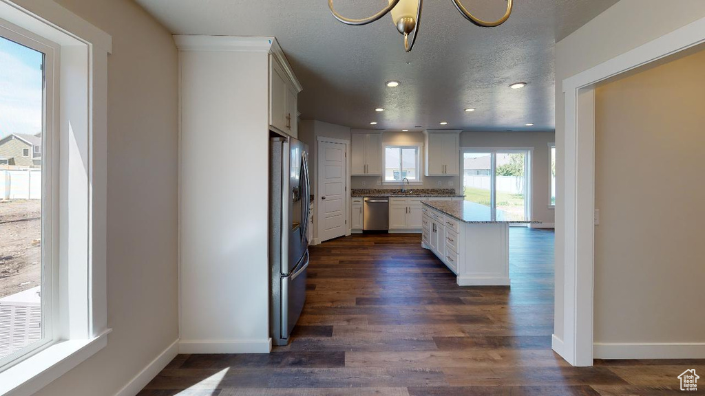 Kitchen with white cabinets, appliances with stainless steel finishes, dark wood-type flooring, and light stone countertops