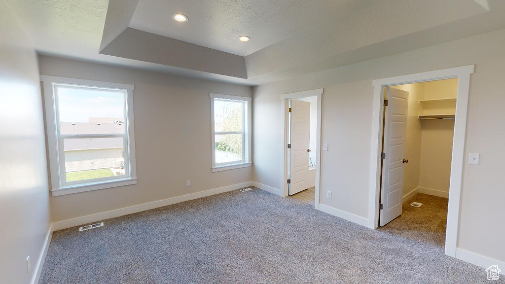 Unfurnished bedroom featuring a textured ceiling, a walk in closet, a closet, a tray ceiling, and light colored carpet