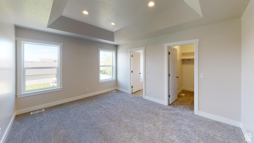 Unfurnished bedroom with a tray ceiling, a spacious closet, light colored carpet, and a closet