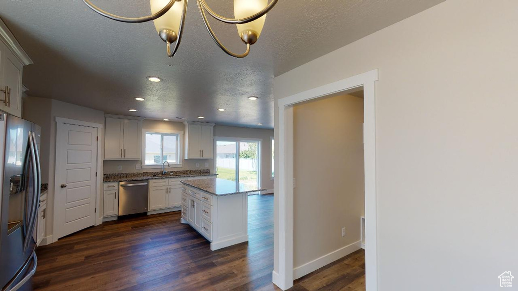 Kitchen featuring appliances with stainless steel finishes, dark wood-type flooring, light stone counters, white cabinets, and a textured ceiling