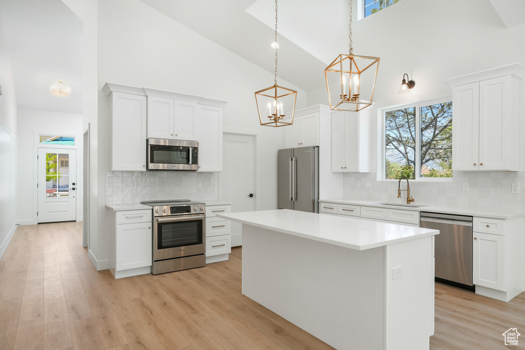 Kitchen with hanging light fixtures, white cabinets, stainless steel appliances, and high vaulted ceiling