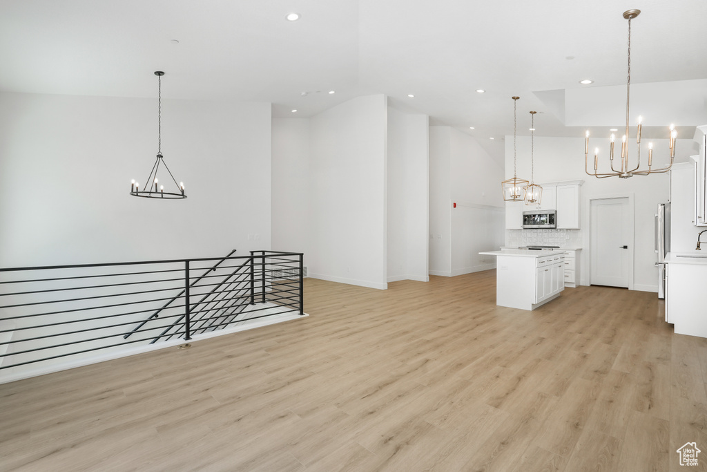 Kitchen featuring white cabinets, hanging light fixtures, a center island, a notable chandelier, and light hardwood / wood-style floors