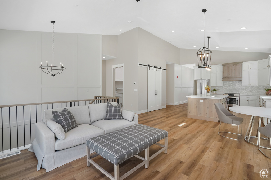 Living room with a barn door, light hardwood / wood-style floors, a chandelier, and high vaulted ceiling