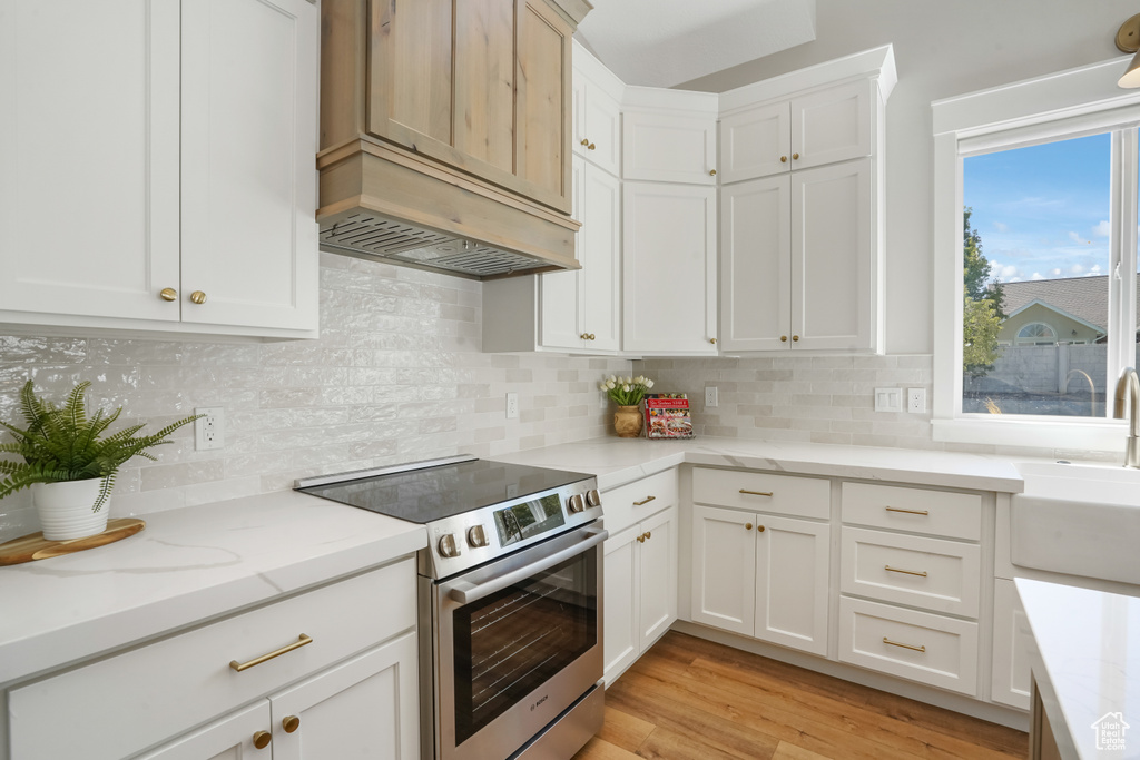 Kitchen with light stone countertops, light wood-type flooring, stainless steel stove, and tasteful backsplash