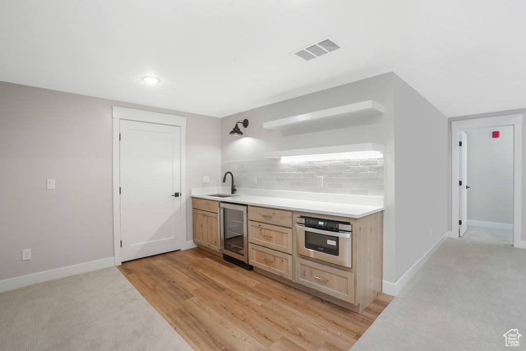 Bar featuring tasteful backsplash, beverage cooler, light hardwood / wood-style flooring, oven, and light brown cabinetry