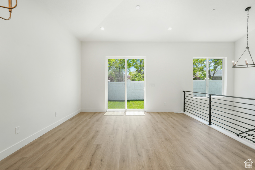 Spare room featuring an inviting chandelier, light hardwood / wood-style flooring, and plenty of natural light