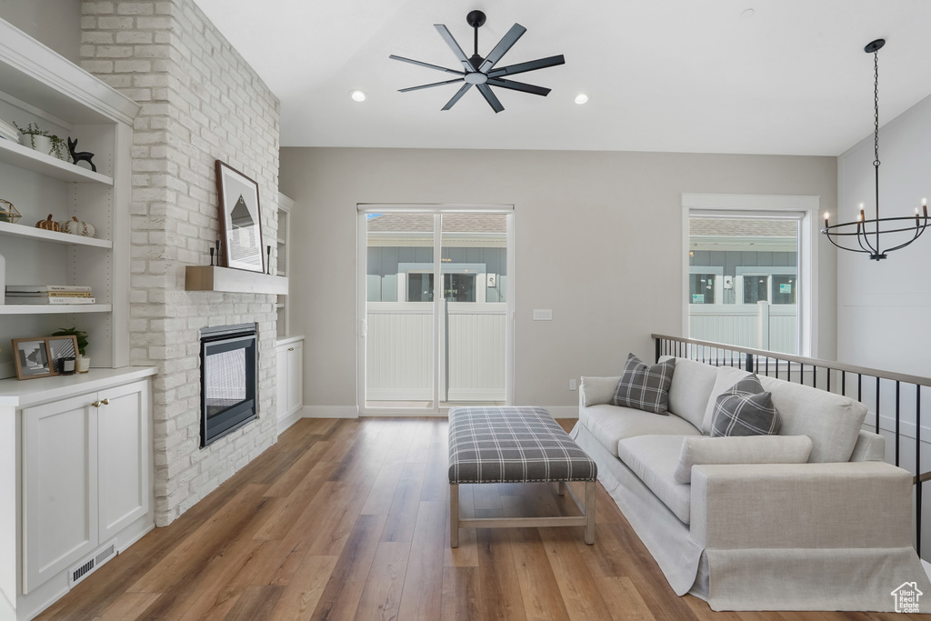 Living room featuring ceiling fan with notable chandelier, a fireplace, hardwood / wood-style floors, and built in features