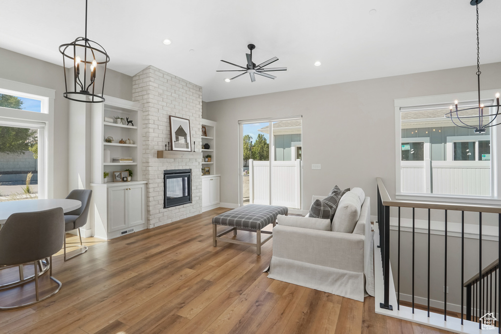 Living room featuring built in shelves, hardwood / wood-style flooring, ceiling fan with notable chandelier, and a large fireplace