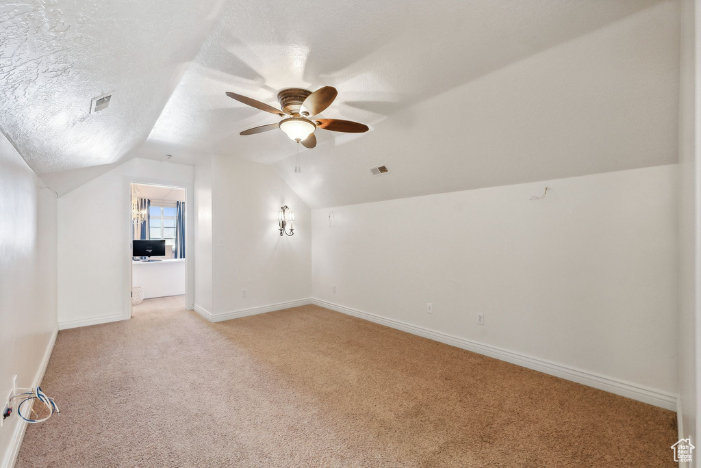 Bonus room featuring a textured ceiling, vaulted ceiling, ceiling fan, and light carpet