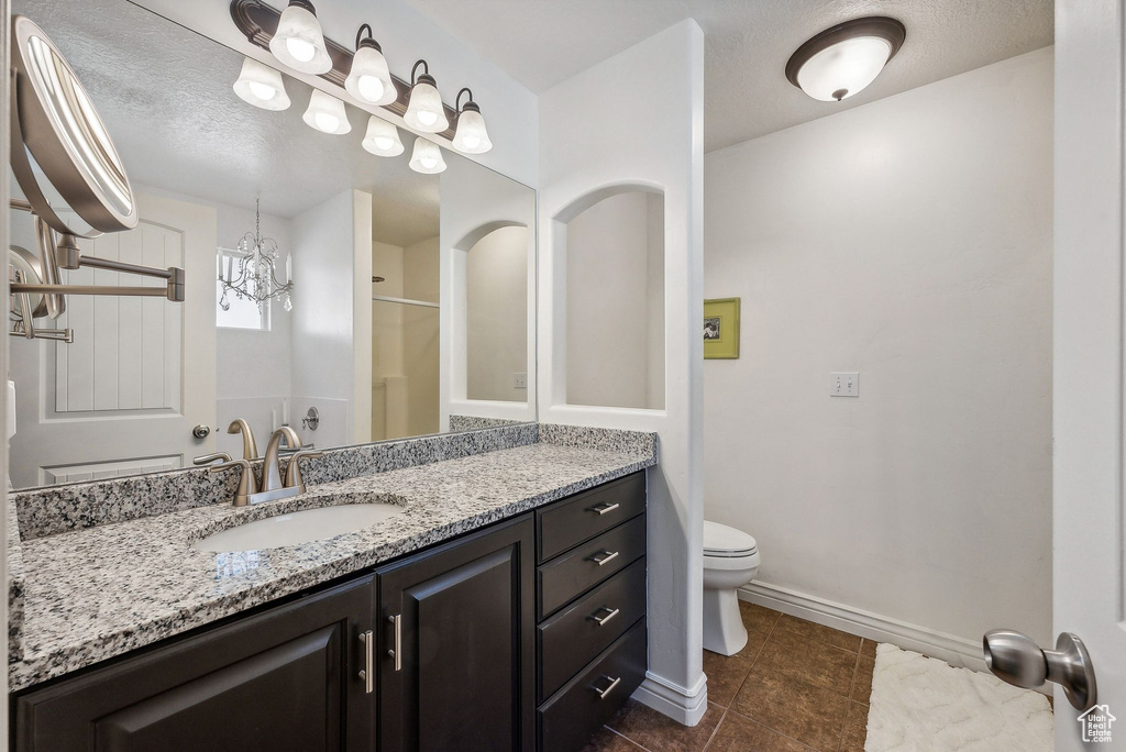 Bathroom featuring a textured ceiling, a shower with door, toilet, and vanity